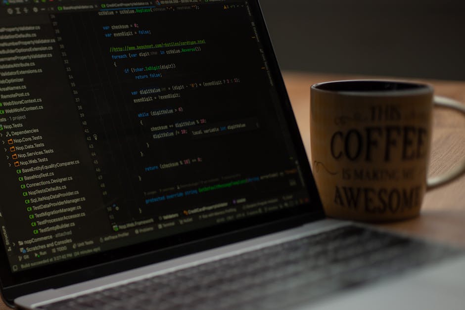 A close-up view of a laptop keyboard and screen displaying lines of code in a programming environment, positioned on a wooden desk. Next to the laptop, there is a ceramic coffee mug with a beige backg